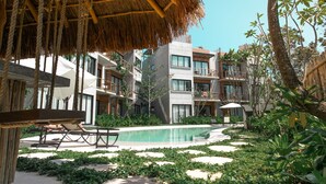 A pool area with lounge chairs, a thatched roof, and modern buildings with balconies. - Macondo Tulum  (Tulum)
