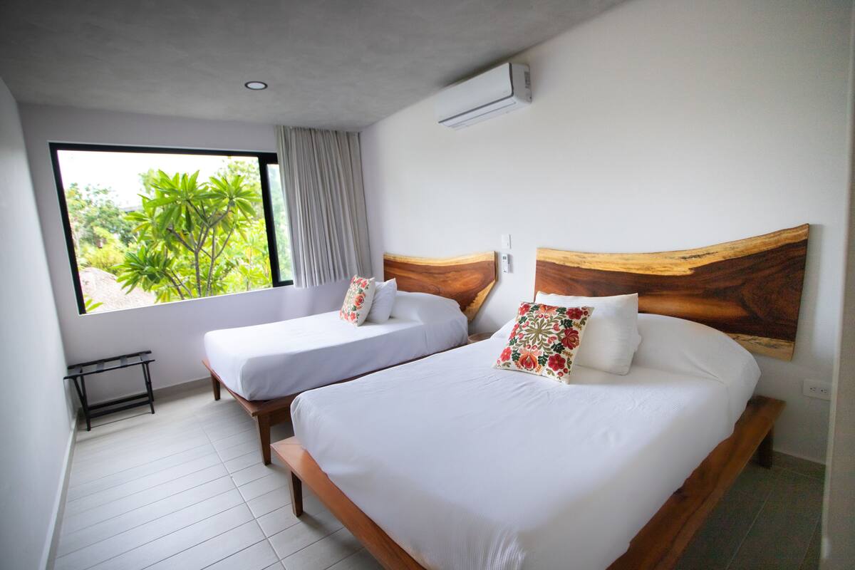 Habitación de hotel con dos camas, una mesita y un ventanal con vistas a zonas verdes.