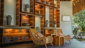 A modern interior with wooden shelving displaying decorative items, wicker chairs, and a thatched roof ceiling. - Macondo Tulum  (Tulum)
