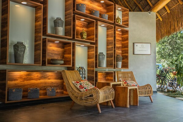 A modern interior with wooden shelving displaying decorative items, wicker chairs, and a thatched roof ceiling. - Macondo Tulum  (Tulum)