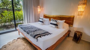 A bedroom with a large bed, a wooden headboard, two bedside lamps, and a view of greenery outside. - Macondo Tulum  (Tulum)