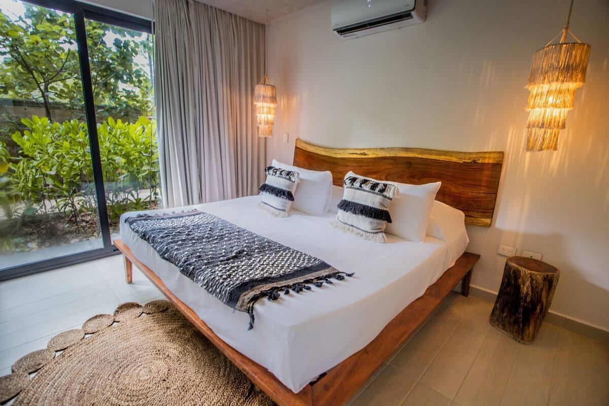Un dormitorio con una cama grande, cabecera de madera, dos lámparas de noche y vistas a zonas verdes.