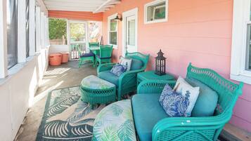 A covered porch with green wicker furniture, including a sofa and chairs, and a patterned rug.