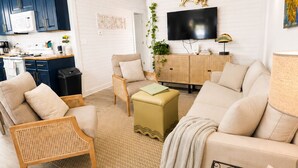 Un salon moderne avec un canapé, un fauteuil et une table basse, une cuisine avec des meubles bleus et un téléviseur à écran plat fixé au mur.