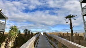 Une promenade en bois menant à une plage, avec un palmier et une clôture.