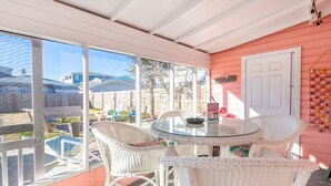 Une terrasse couverte avec une table ronde en verre et des chaises en osier blanc.