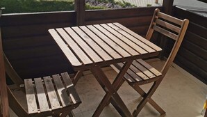 En träveranda med ett bord och stolar, med utsikt över en sjö och berg.