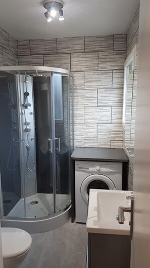A modern bathroom with a glass shower enclosure, a built-in washing machine, and a toilet.