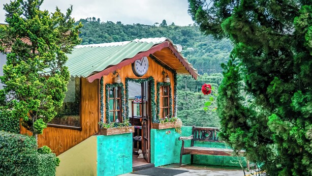 A wooden cabin with a clock on the front, a bench, and a door leading inside. - Pousada Casa de Campos Mountain by Concavus (Campos do Jordão)