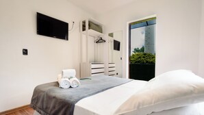 A modern bedroom with a bed, a built-in wardrobe, a flat-screen TV, and a view of greenery through a door. - Pousada Casa de Campos Mountain by Concavus (Campos do Jordão)