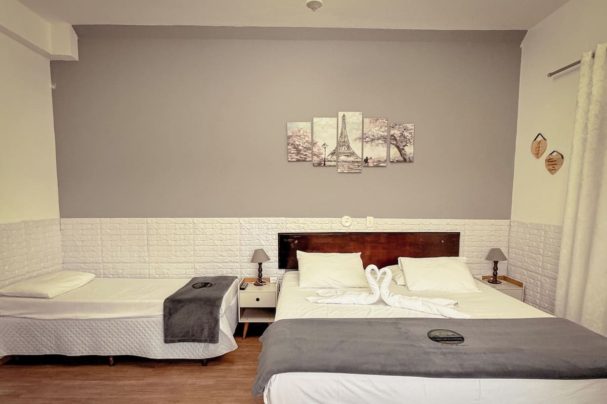 Een hotelkamer met twee bedden, een witte bakstenen muur, een schilderij van de Eiffeltoren en een houten hoofdeinde.