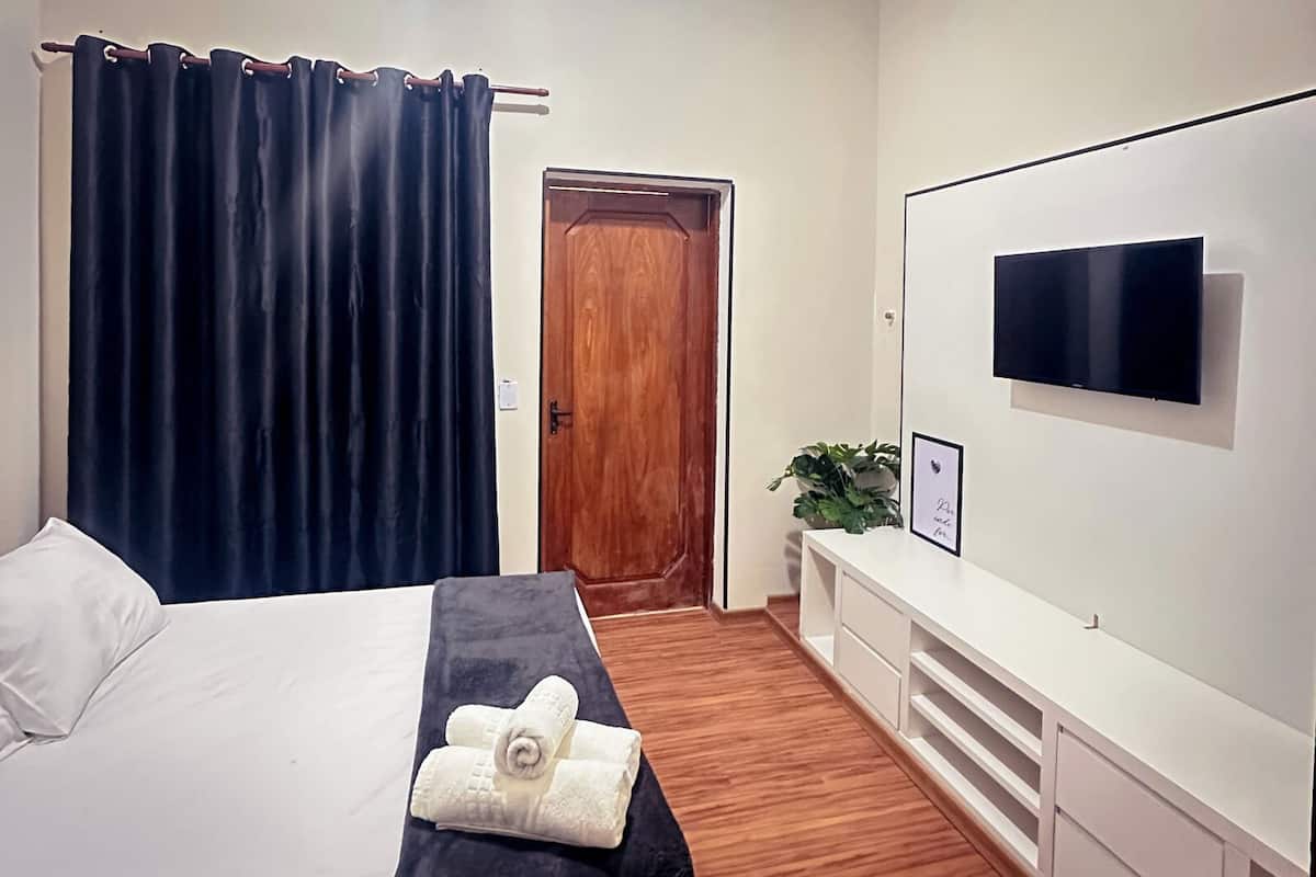 Hotelkamer met een bed, een aan de muur bevestigde televisie, een houten deur en een plant op een witte console tafel.