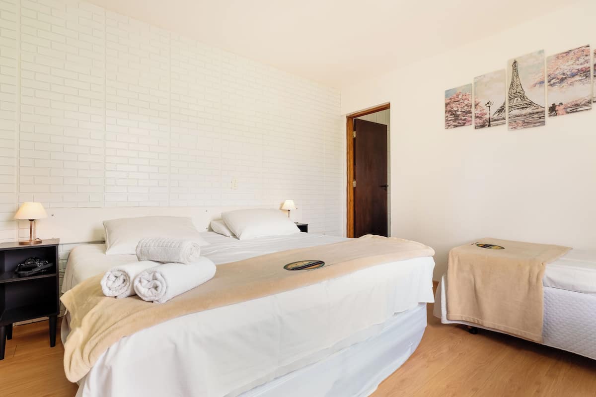 Een hotelkamer met een witte bakstenen muur, een bed met witte lakens, een nachtkastje met een lamp en een klein tafeltje met een handdoek.