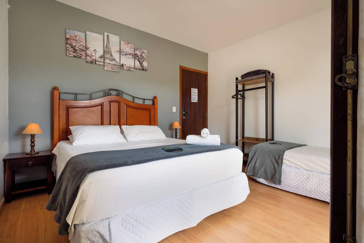Een hotelkamer met een groot bed, een kleiner bed, een houten nachtkastje met een lamp, een deur en een muur met drie ingelijste foto's.