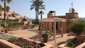 Un patio con una pérgola, plantas en macetas y un banco.
