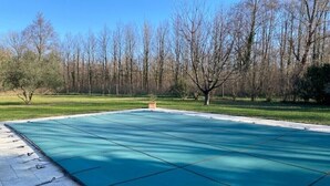 A large, empty swimming pool with a green cover, surrounded by a grassy area and trees. - Mas de Barthe (Avignon)