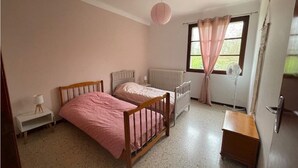 A bedroom with two single beds, a bedside table, a radiator, a window with curtains, and a small wooden stool. - Mas de Barthe (Avignon)