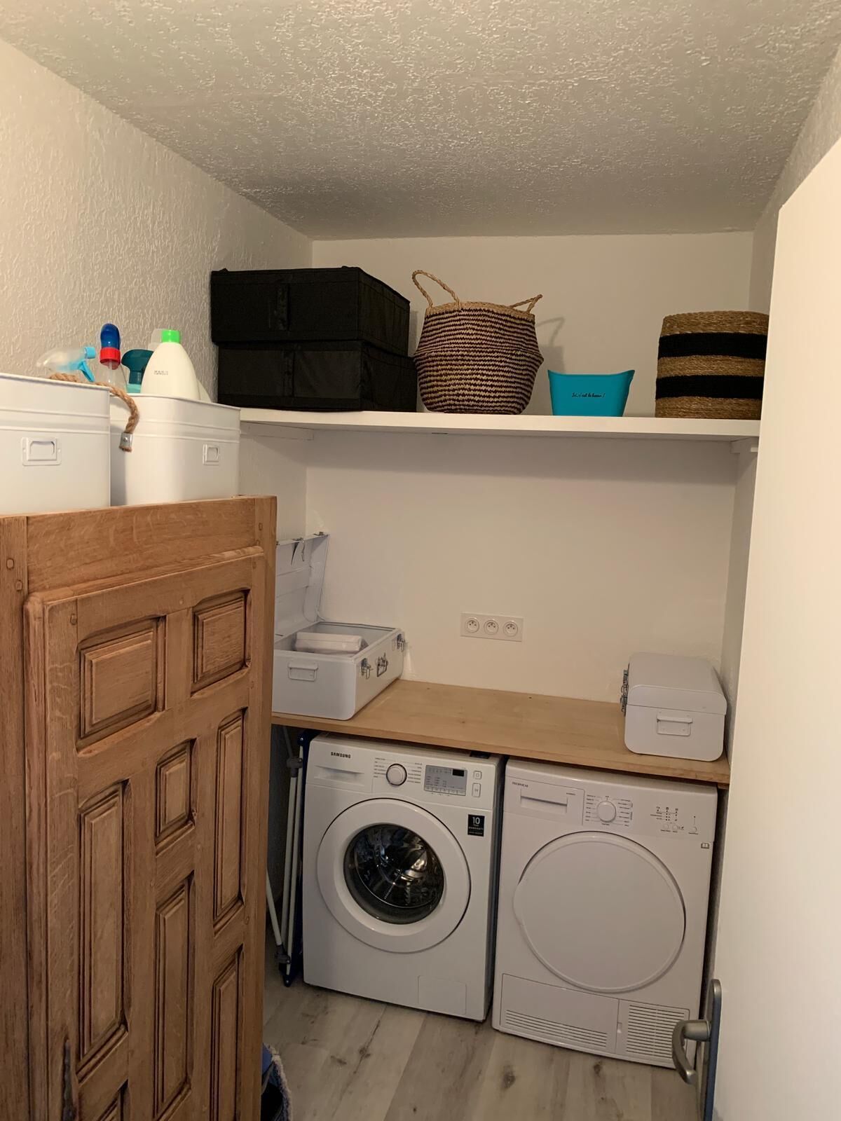 Un lavadero con lavadora, secadora y estantes con cajas y cestas de almacenamiento.