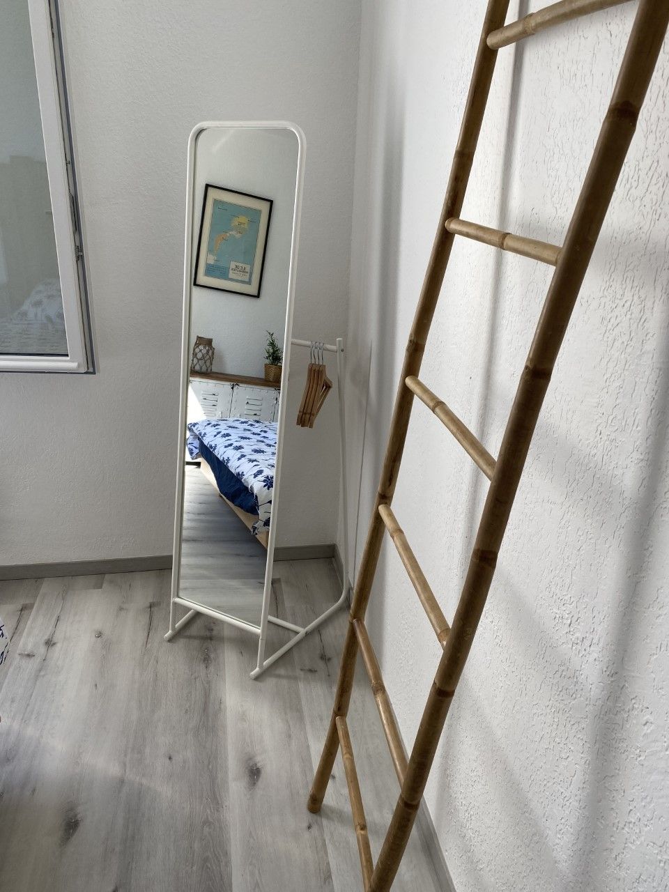 A room with a bed, a wooden ladder, and a white wall with a framed picture.