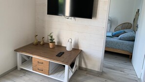 Huoneessa on seinälle asennettu televisio, puinen työpöytä laatikoineen, koriste-esineitä ja kuvioiduilla tekstiileillä varustettu sänky.