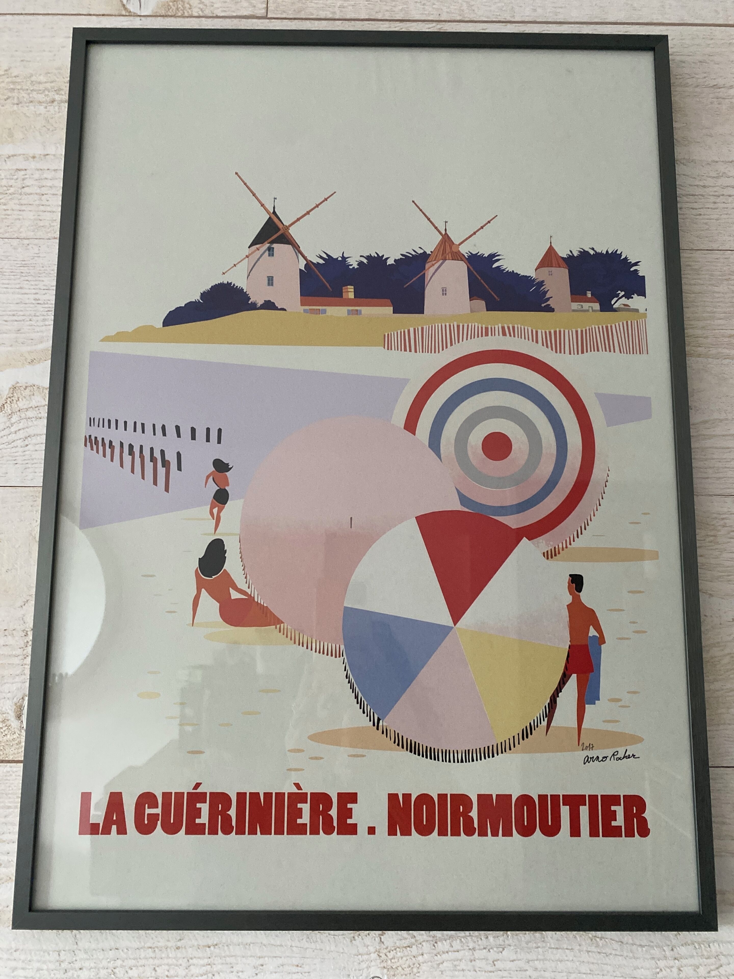 A framed poster with a beach scene, windmills, and people.