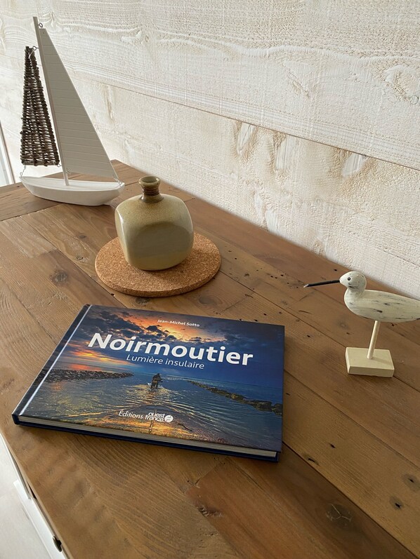 En bok med titeln ”Noirmoutier” ligger på en träyta, bredvid en keramikvas, en liten modell av en segelbåt och en fågelfigur.