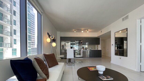 Un salon moderne avec un canapé, une table basse et une vue sur la ville grâce à de grandes fenêtres.