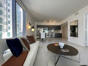 A modern living room with a sofa, a coffee table, and a view of the city through large windows.