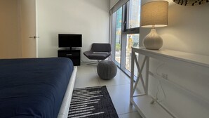 Une chambre moderne avec un lit, une télévision, une chaise, une lampe et une grande fenêtre.