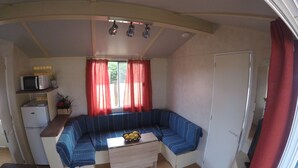 A compact living space with a blue sofa, a small table with a fruit bowl, a microwave, and a refrigerator. - Casa La Abuela María (Vejer de la Frontera)