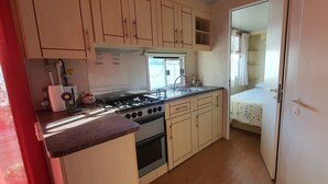 A compact kitchen with a gas stove, oven, and sink. There is a bed with a window and a door leading to a shower. - Casa La Abuela María (Vejer de la Frontera)
