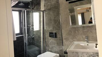A modern bathroom with a glass-enclosed shower, a toilet, and a sink with a marble countertop.