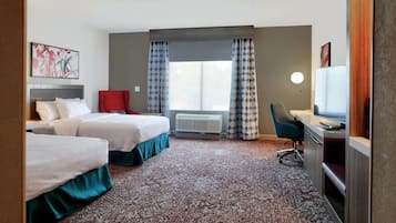 A hotel room with two beds, a desk with a TV, a red chair, a large window with patterned curtains, and a wall-mounted air conditioner.