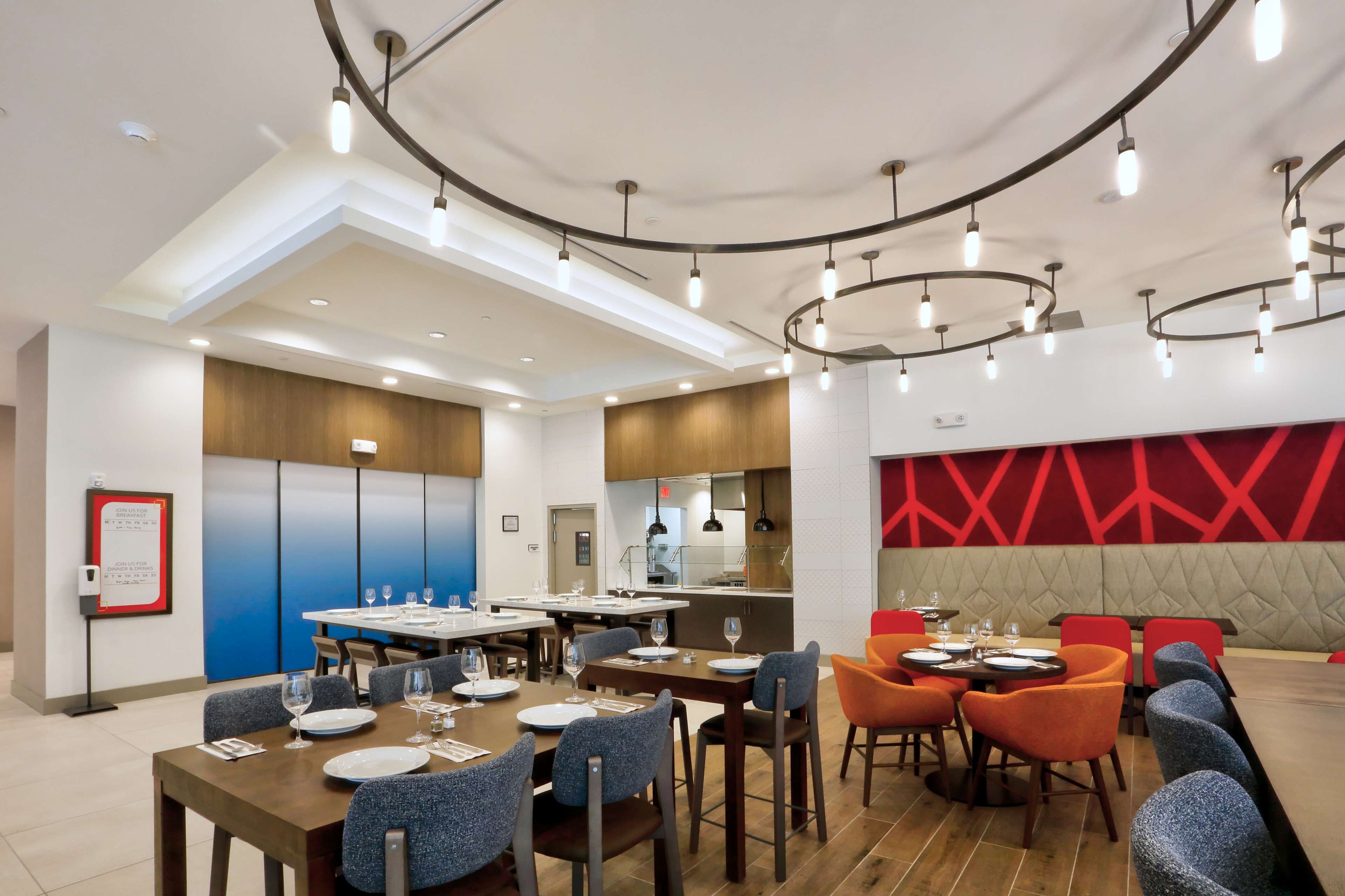 Un espace repas moderne avec des tables rondes, des chaises bleues et orange, et une cuisine en arrière-plan.