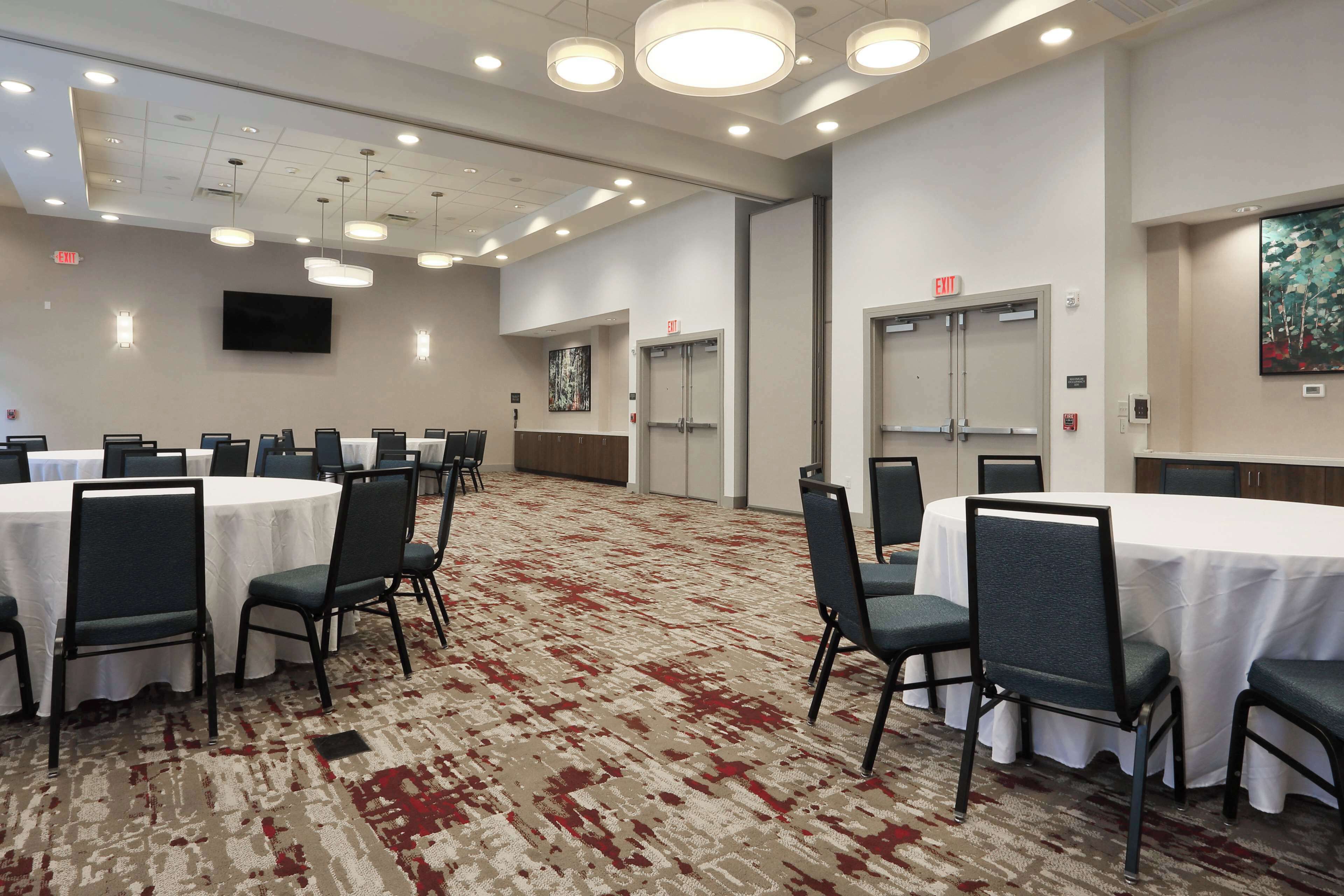 Un salón de conferencias con mesas redondas, sillas y piso alfombrado.