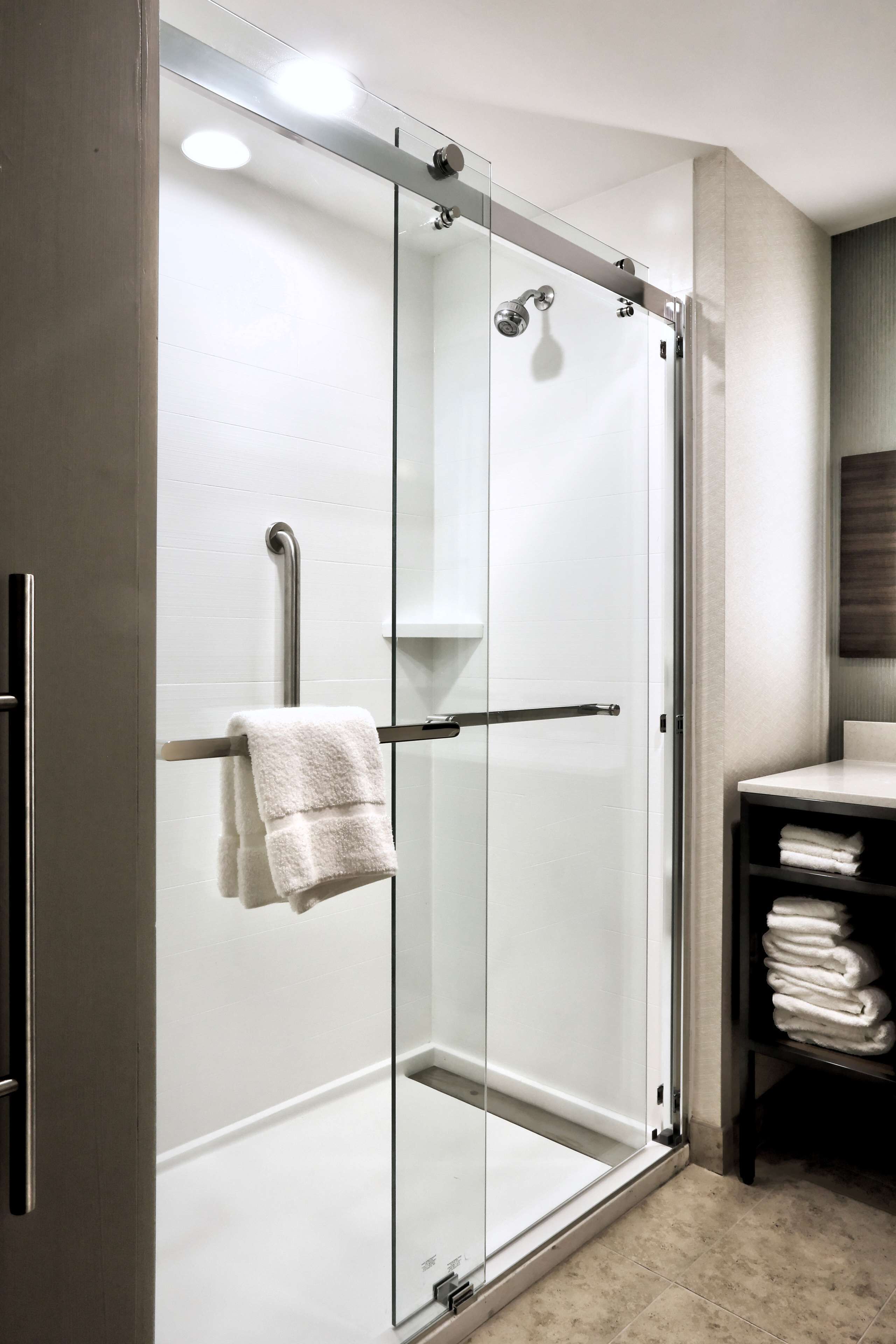 Un baño moderno con cabina de ducha de vidrio, un perchero y una pila de toallas en un estante.