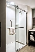 Un baño moderno con cabina de ducha de vidrio, un perchero y una pila de toallas en un estante.