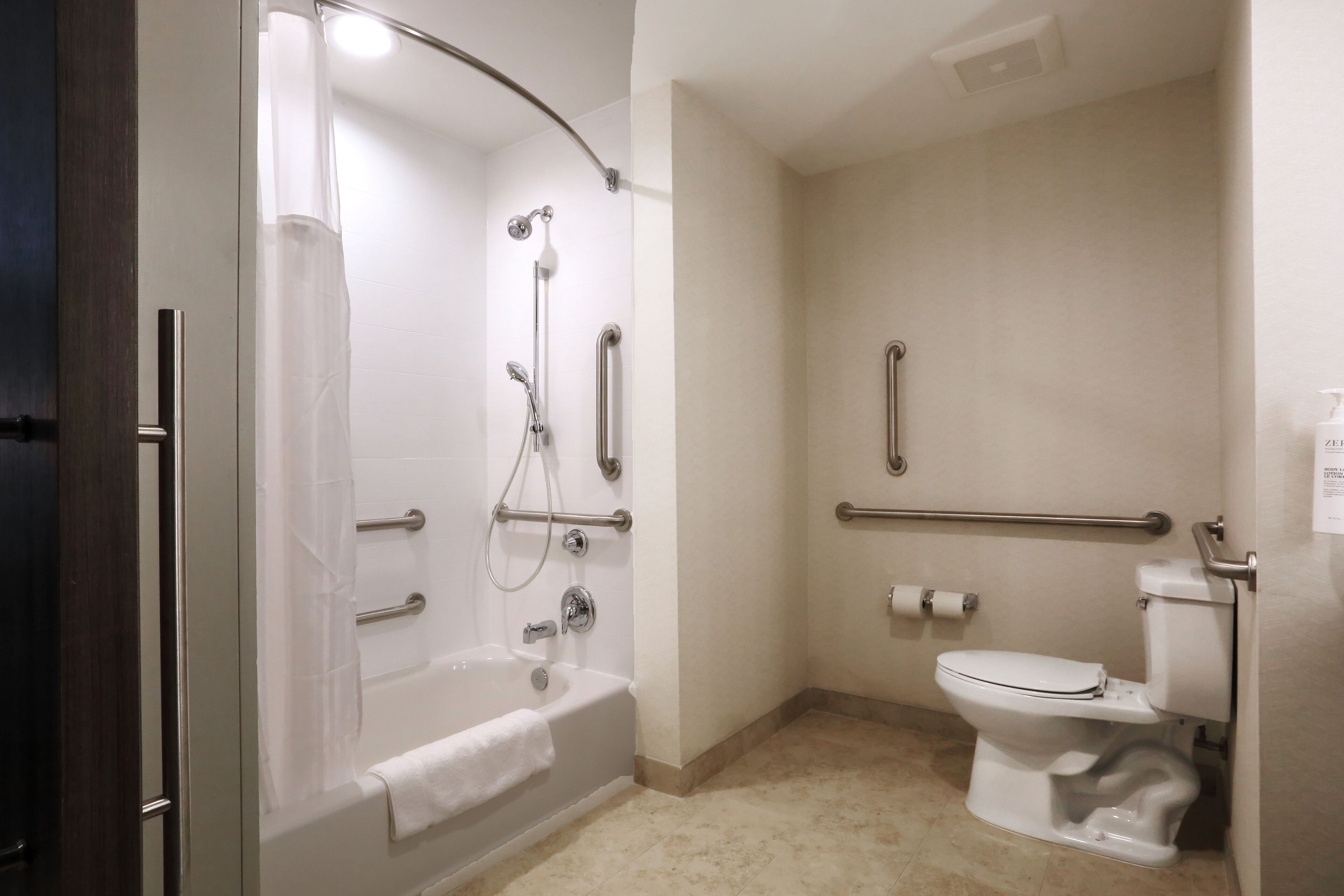 A bathroom with a bathtub, toilet, and grab bars.