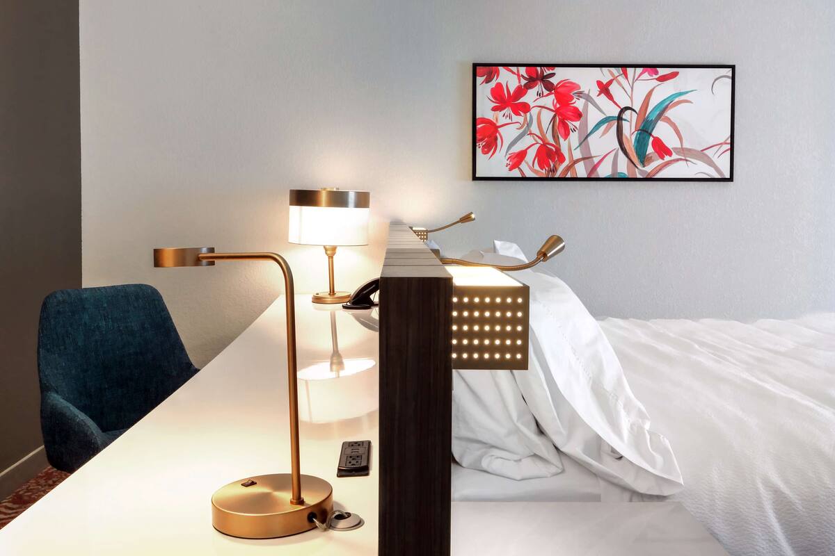 Hotellihuone, jossa on sänky, kirjoituspöytä lampun kanssa, tuoli ja seinään kiinnitetty puhelin.
