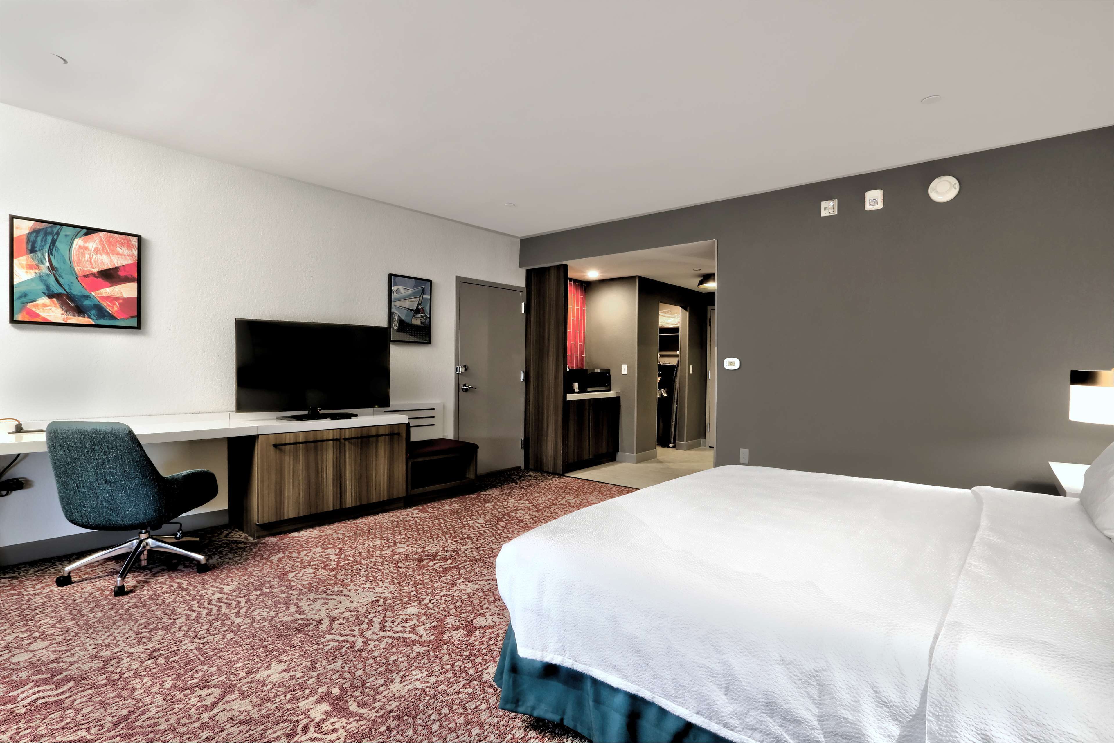 Une chambre d’hôtel équipée d’un lit, d’un bureau, d’une chaise, d’une télévision et d’œuvres d’art accrochées au mur.