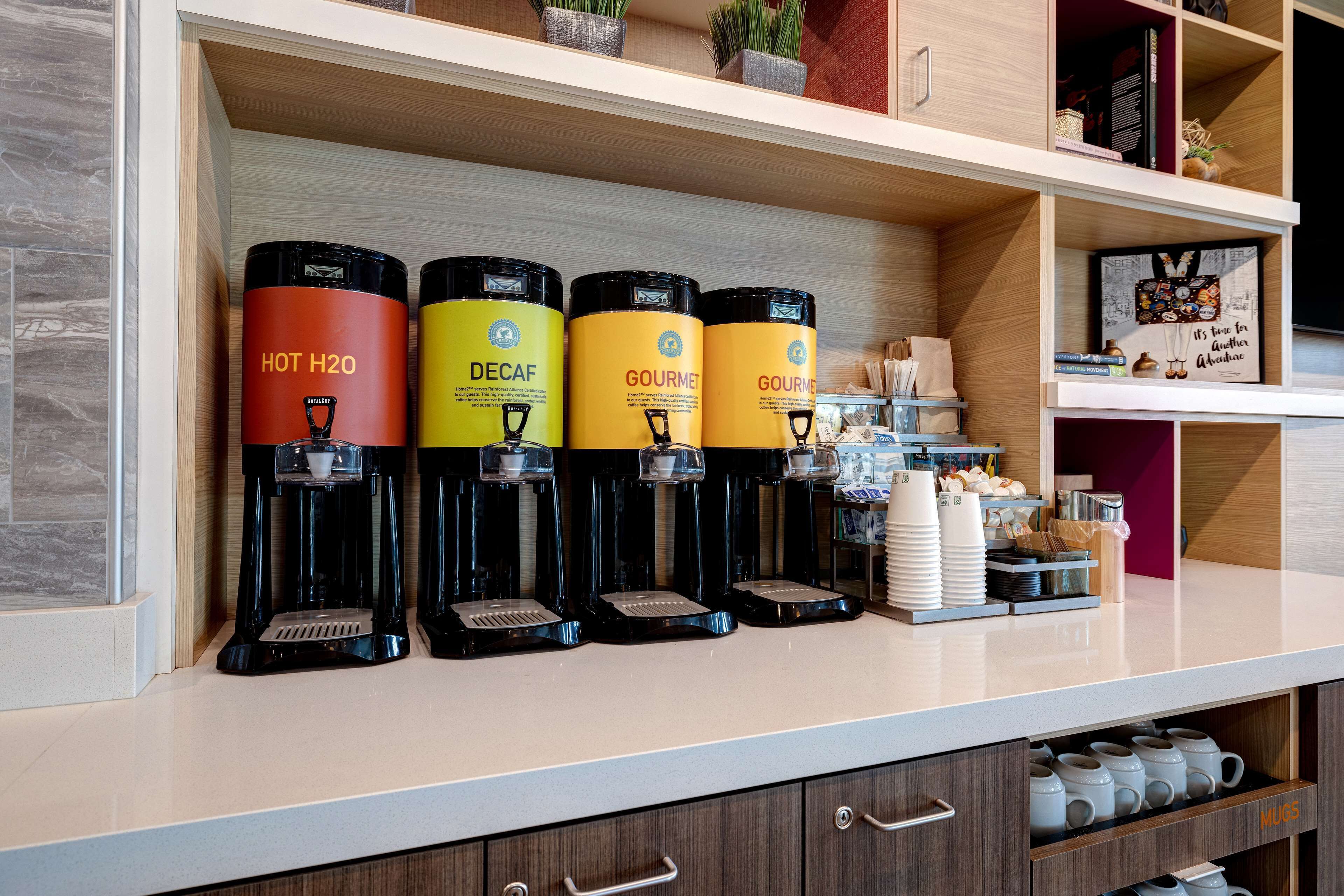 Una estación de café con cuatro dispensadores etiquetados como AGUA CALIENTE, DESCAFEINADO y CAFÉ ESPECIAL.