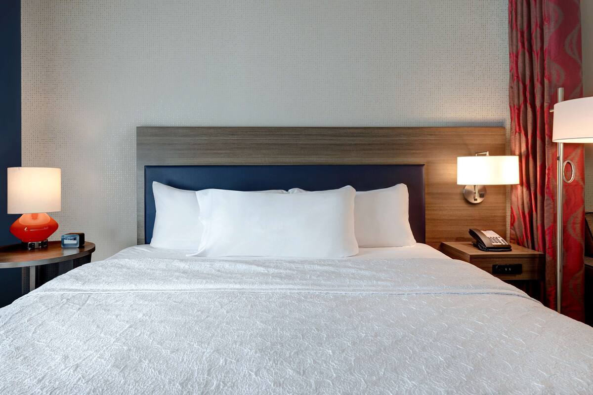 A neatly made bed with white linens and a wooden headboard, two bedside lamps, and a nightstand with a telephone.