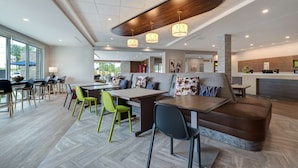 A modern restaurant with a wooden ceiling, green and black chairs, and a central seating area with a sofa and table. - Home2 Suites Downtown Nashville/Metrocenter (Nashville)