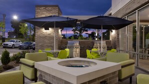 An outdoor patio with a stone fire pit, green chairs, and two barbecue grills. - Home2 Suites Downtown Nashville/Metrocenter (Nashville)