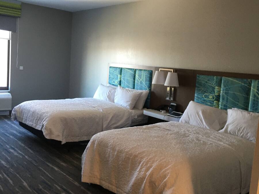 Quarto de hotel com duas camas, uma mesa de cabeceira e uma janela.