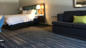 Habitació d'hotel amb un llit, una tauleta de nit, una làmpada, un sofà i un quadre a la paret.