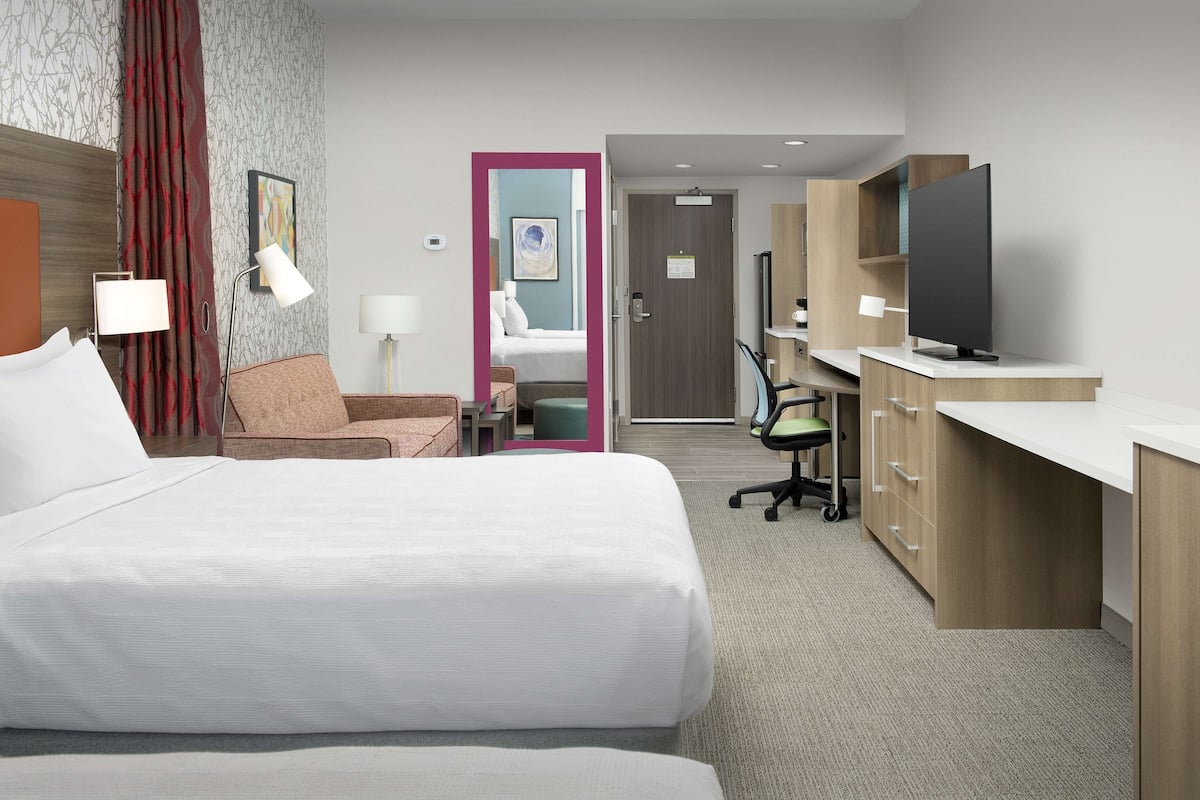 Hotelkamer met twee bedden, een bureau, een flatscreen televisie, een stoel, een bureaulamp en een badkamer zichtbaar door een geopende deur.