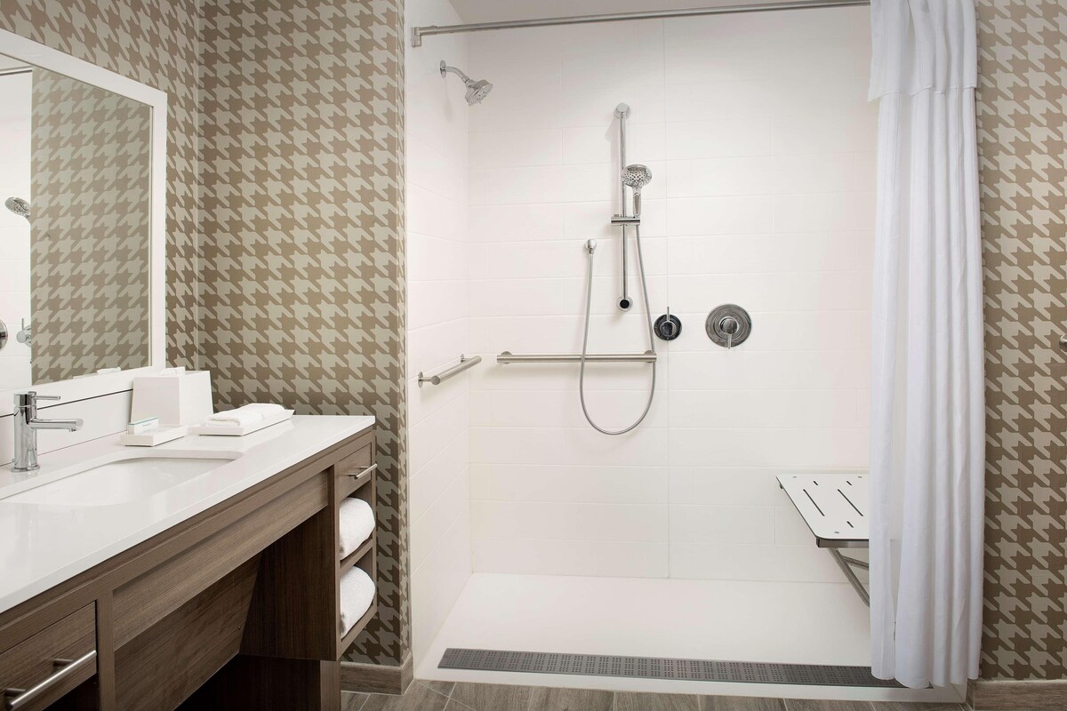 Een moderne badkamer met een douche, wastafel en opbergmeubel.