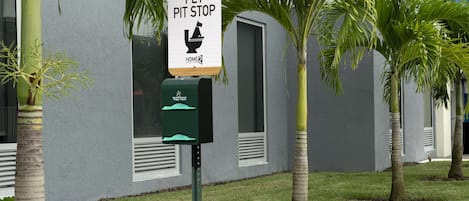 A sign for a pet pit stop and a trash can in front of a building with palm trees.