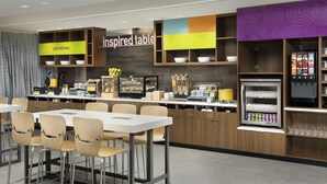 A modern breakfast area with a self-service station, seating, and a refrigerator stocked with beverages.